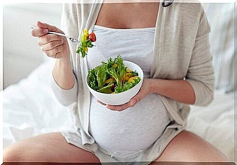 pregnant woman sitting on bed eats salad