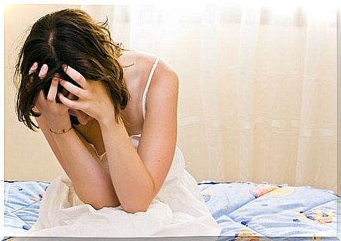 girl holds head in her hands sitting on bed