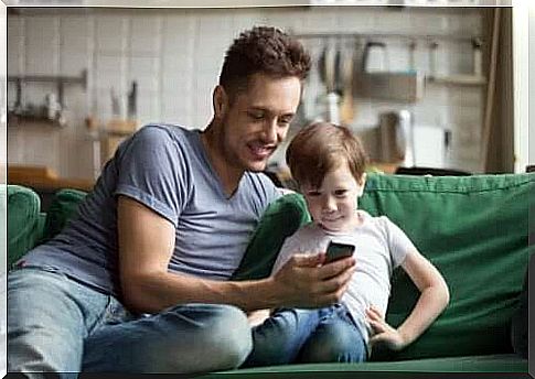 Father and son sitting on the sofa using an app on the phone.