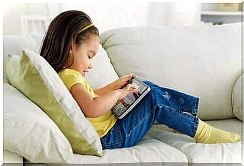 Little girl sitting on the sofa using a tablet to play.