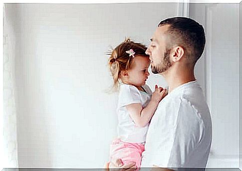 Father holding newborn daughter in his arms and giving her a kiss.