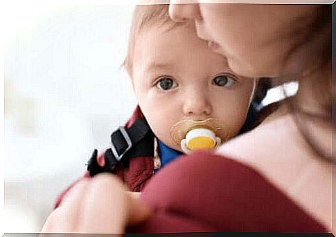 Baby in mother's arms with pacifier in mouth.